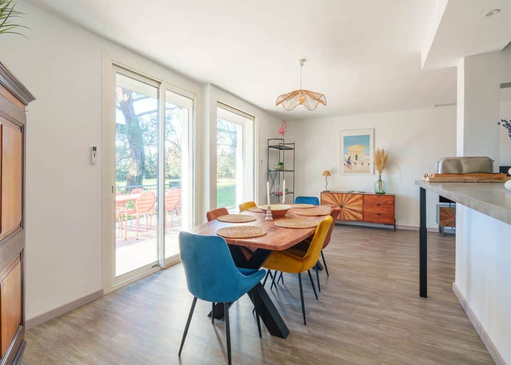 Salon lumineux d’une location saisonnière avec cuisine ouverte et table en bois