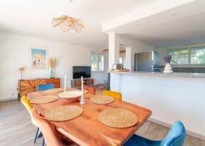 Salon lumineux d’une location saisonnière avec cuisine ouverte et table en bois