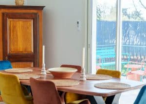 Salon lumineux d’une location saisonnière avec cuisine ouverte et table en bois