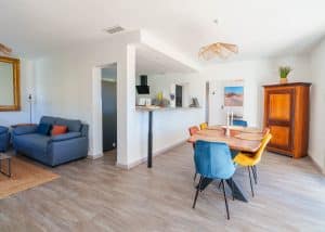 Salon lumineux d’une location saisonnière avec cuisine ouverte et table en bois