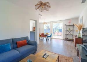 Salon lumineux d’une location saisonnière avec cuisine ouverte et table en bois