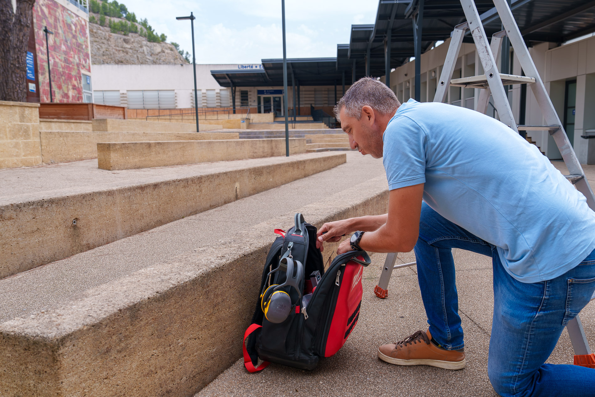 Technicien BS Solutions agenouillé près de son sac d’outillage, à côté d’une échelle en extérieur.