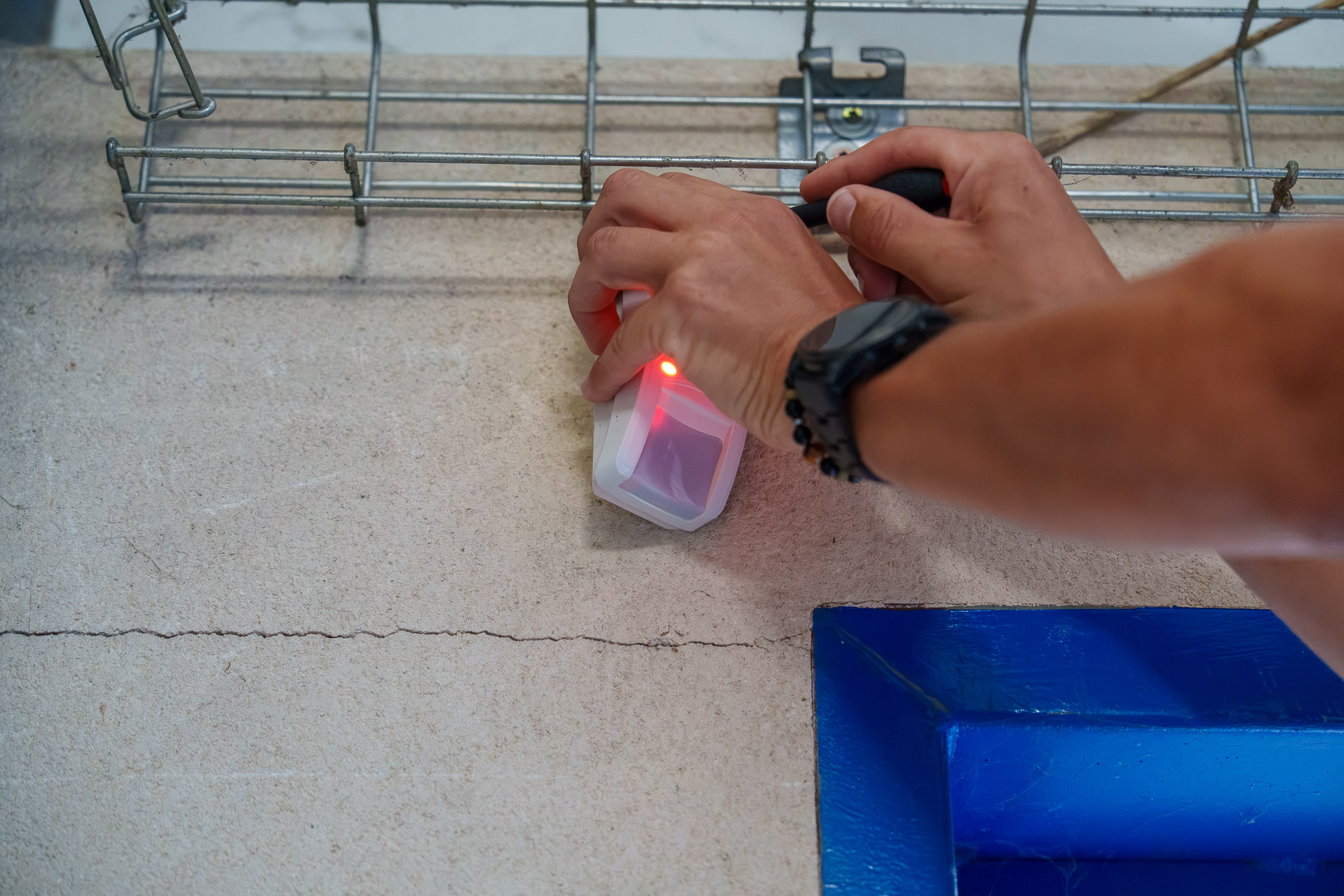 Mains d’un technicien intervenant sur un détecteur de mouvement fixé au mur, voyant rouge allumé.